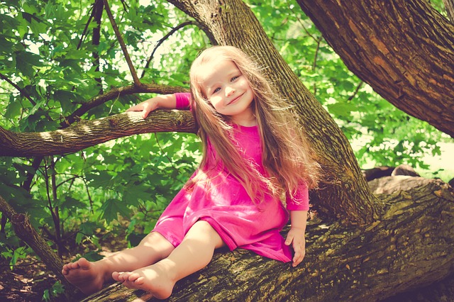 Malá slečna na stromě v růžových šatičkách, s dlouhými vlásky a s širokým úsměvem.jpg