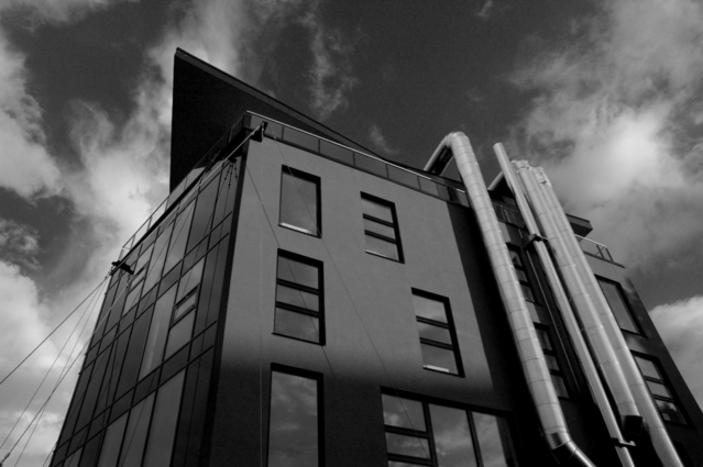 Černobílá fotografie budovy pohled nahoru, na jedné straně velké roury