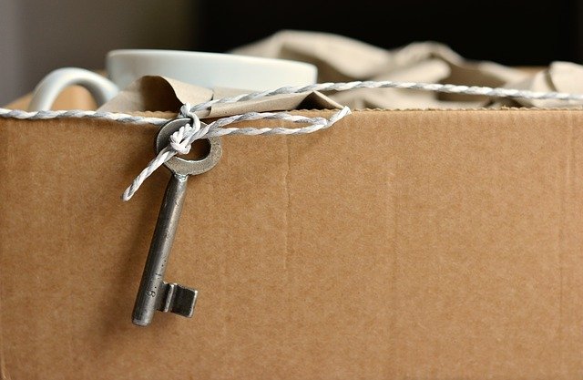 Stěhování-papírová krabice s nádobím, kolem krabice připevněný provázek s klíčem od bytu