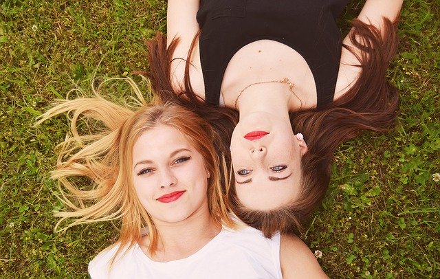 bruneta a blondýna ležící na zelené trávě